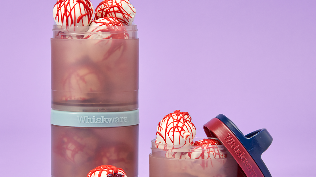 A whiskware snacking container with the top jar removed and filled with cake balls coated in white icing and drizzled with red to look like blood splatter.