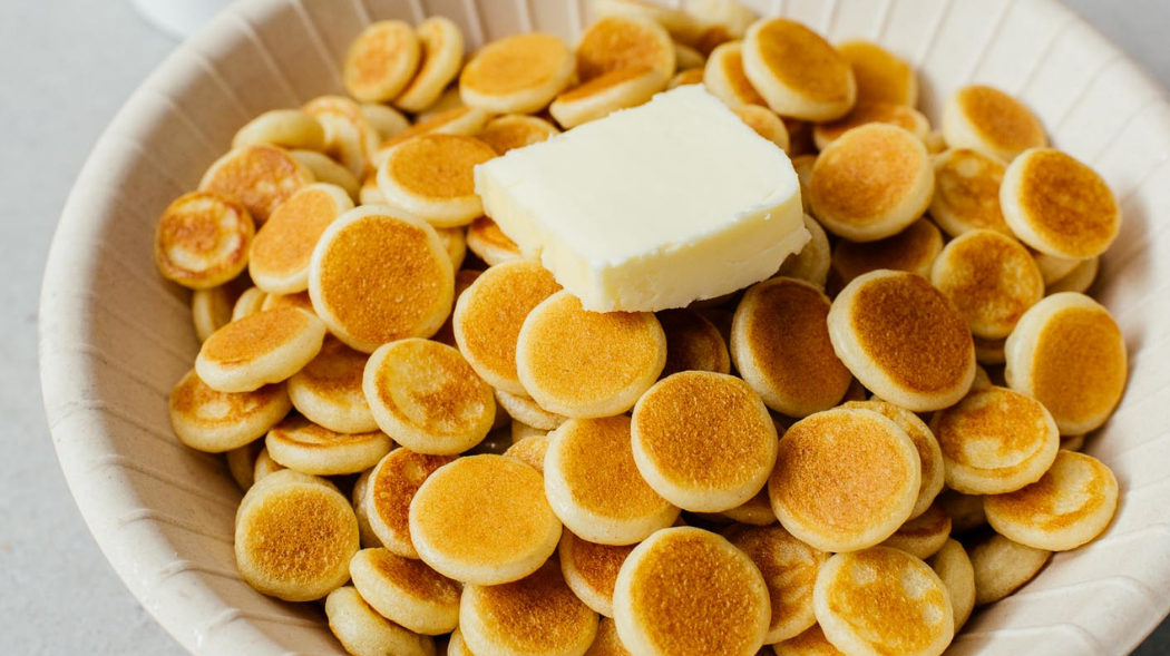 a bowl of very small pancakes, about the size of a quarter, with a pad of butter sitting on top.