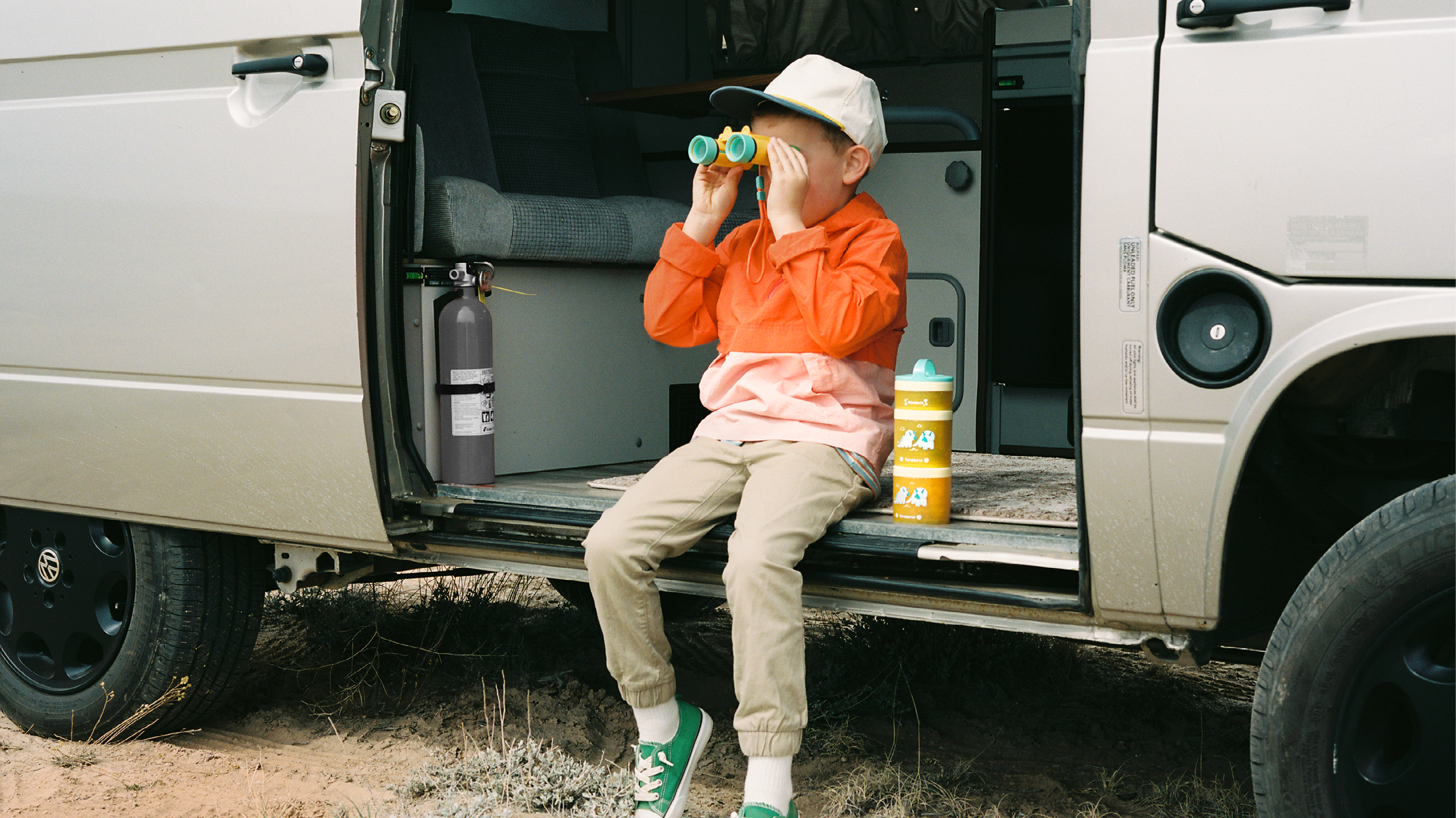 Boy sitting on the floor of an open van door looking out of the car with binoculars.