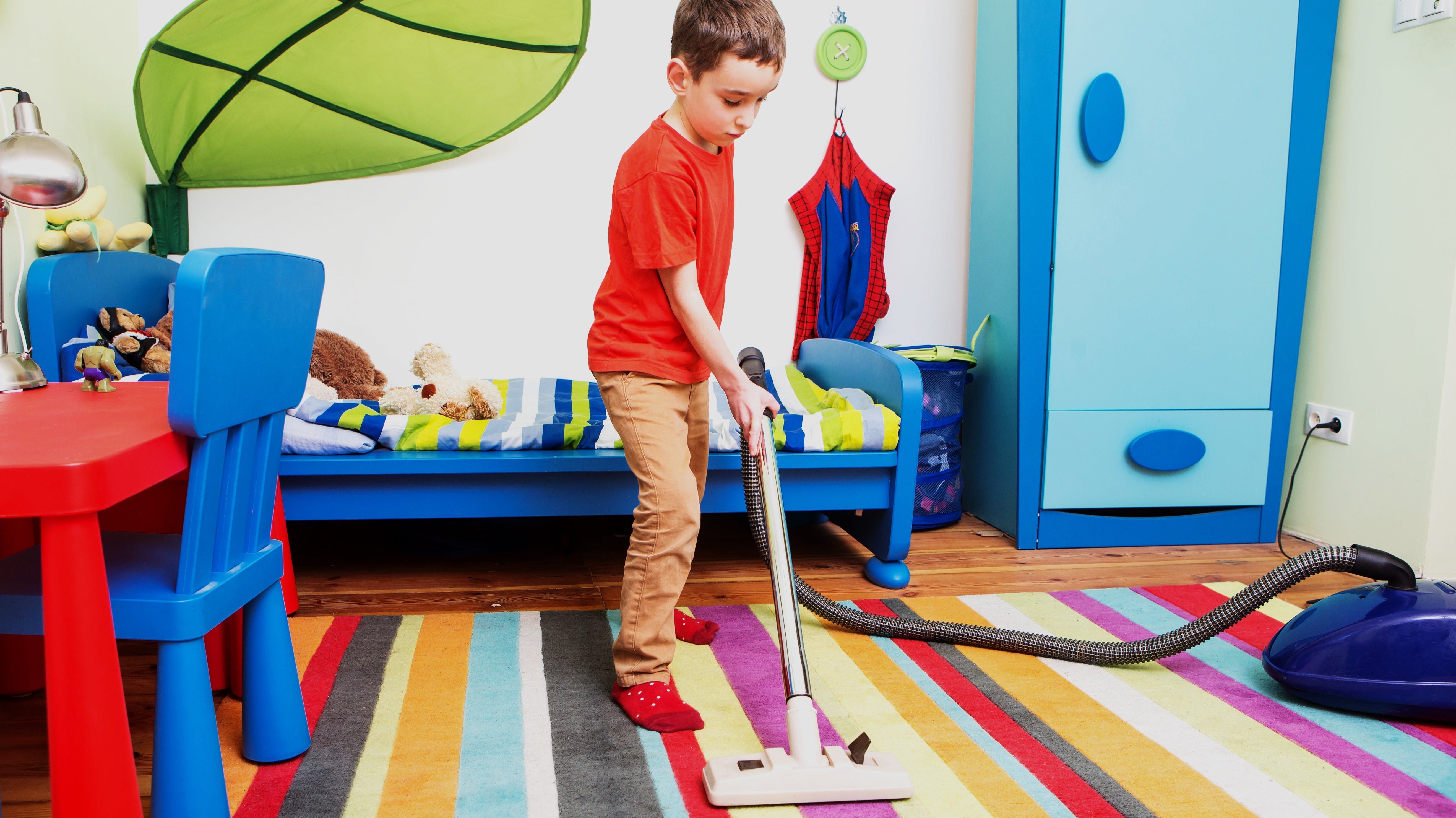 A young boy vacuums a colorful rug in a play room.