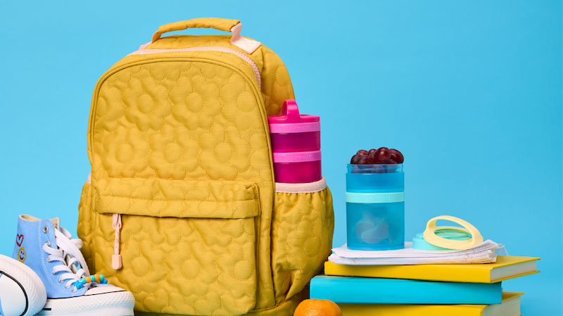 Backpack with books, sneakers, and Whiskware Snack Containers in front of a blue background.