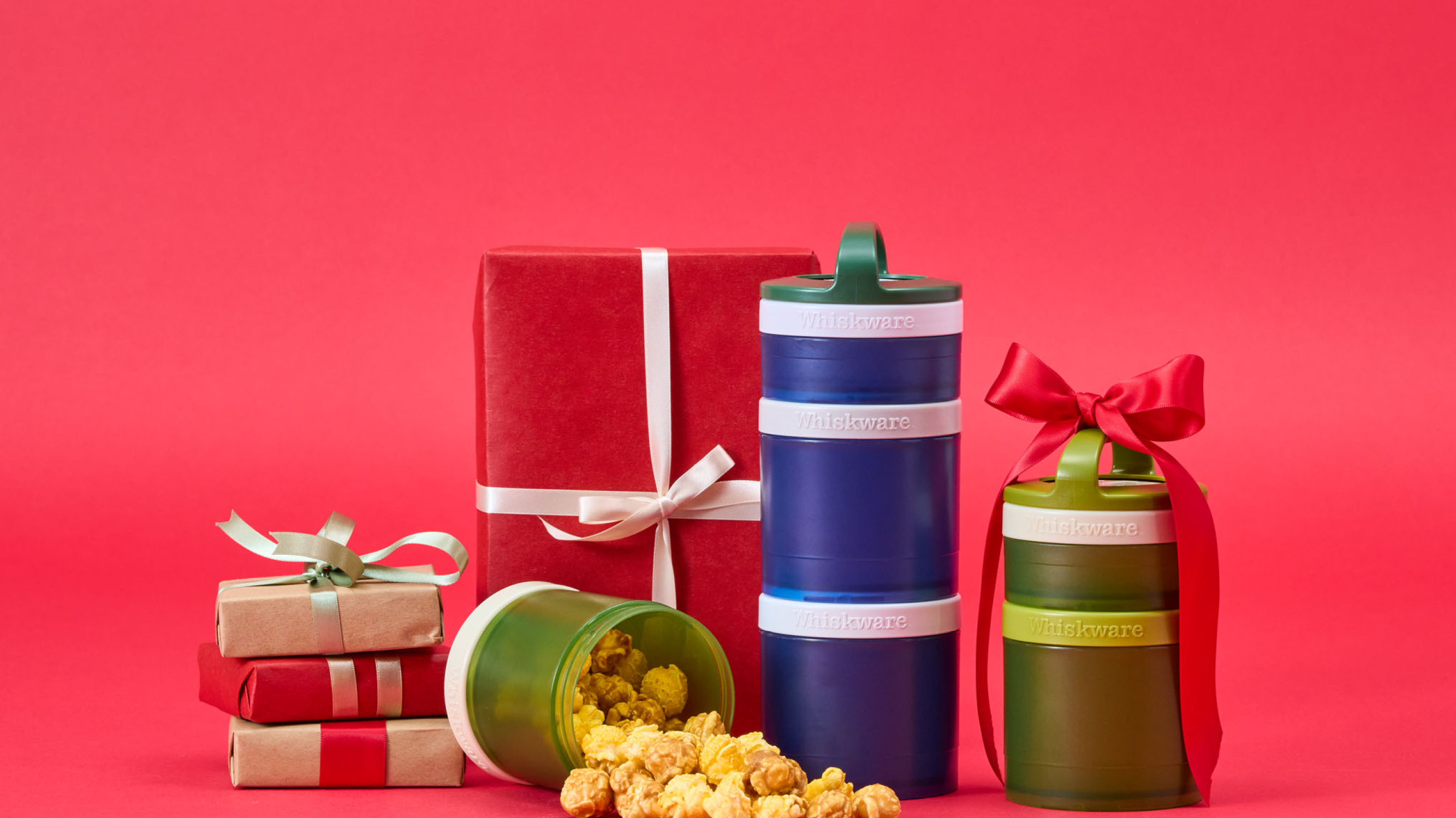 Whiskware containers filled with popcorn and wrapped gifts on a red background.