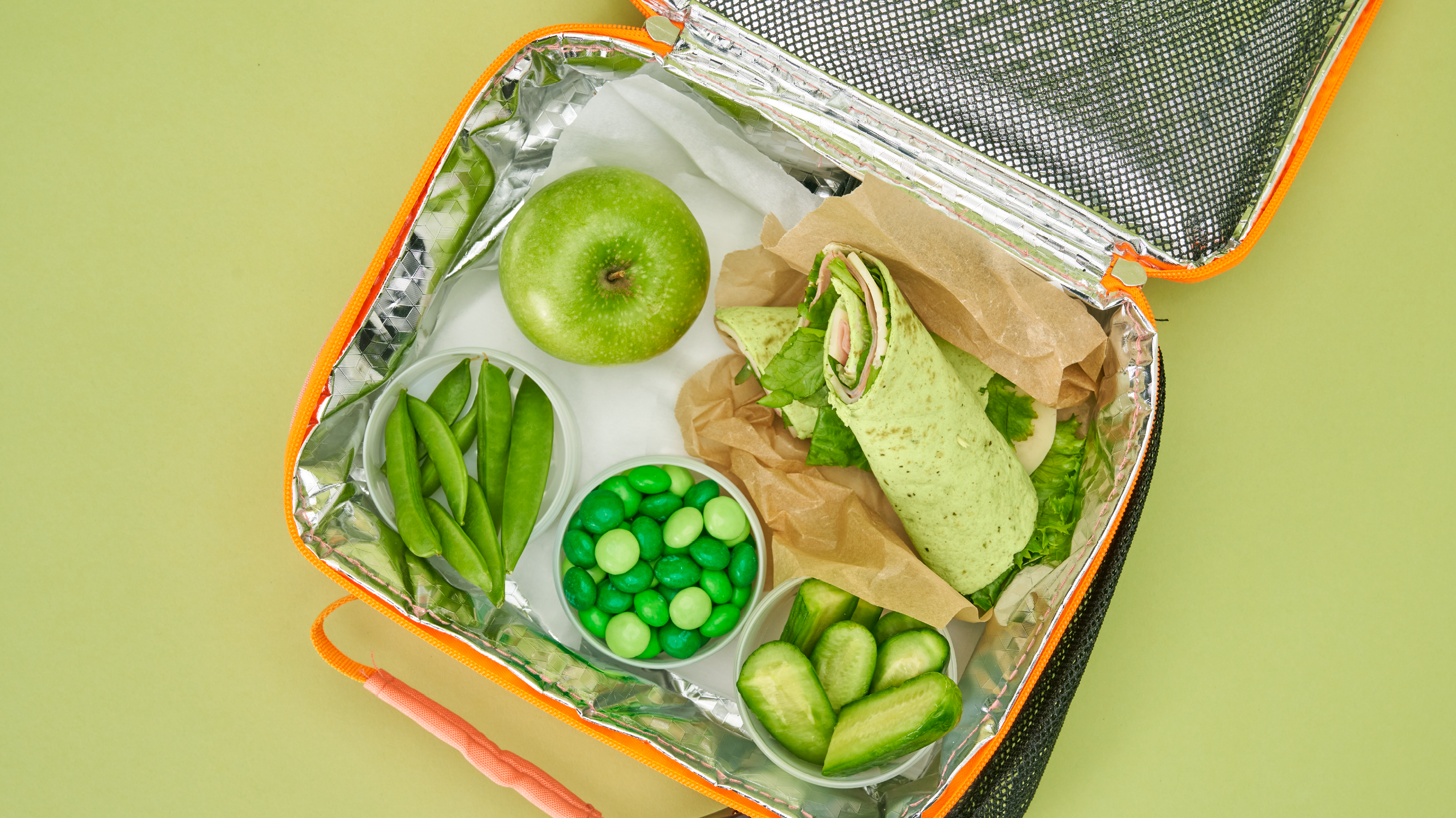 School lunchbox with wrap, apples, peas, pickles, and M&Ms
