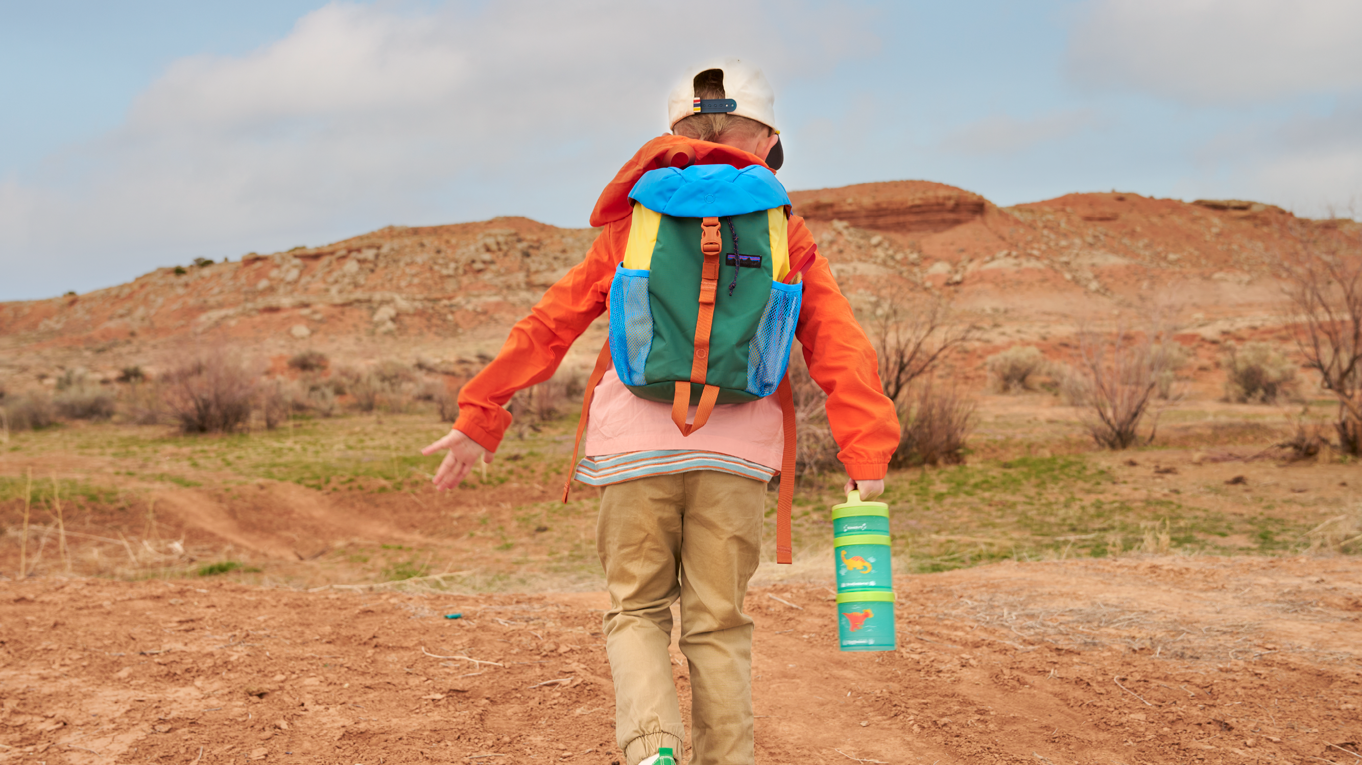 Boy with backpack and Whiskware snack container running on an outdoor red rock trail.