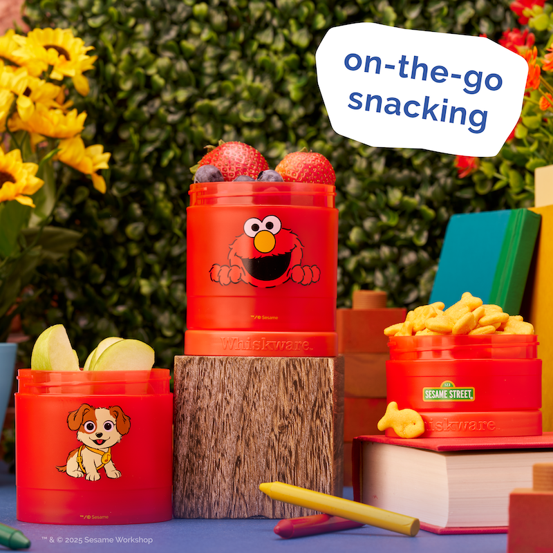 Red snack containers with cartoon characters on a blue surface with flowers and books in the background, labeled 'on-the-go snacking'.