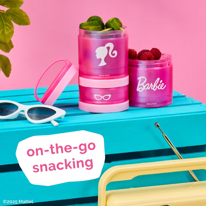 Pink snack containers with Barbie logo on a blue surface with sunglasses and berries, featuring the text 'on-the-go snacking'.