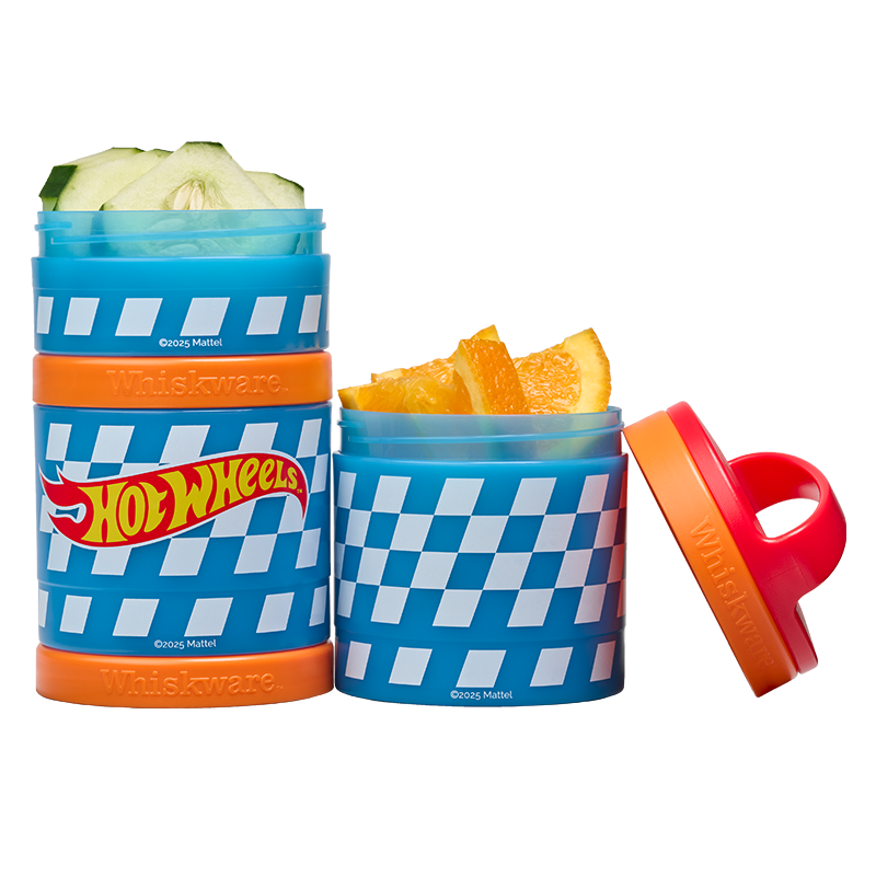 Two snack containers with checkered design and Hot Wheels branding, one containing cucumbers and the other with oranges.