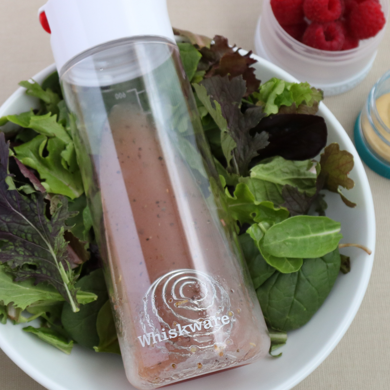 A whiskware dressing shaker laying on a bed of lettuce.