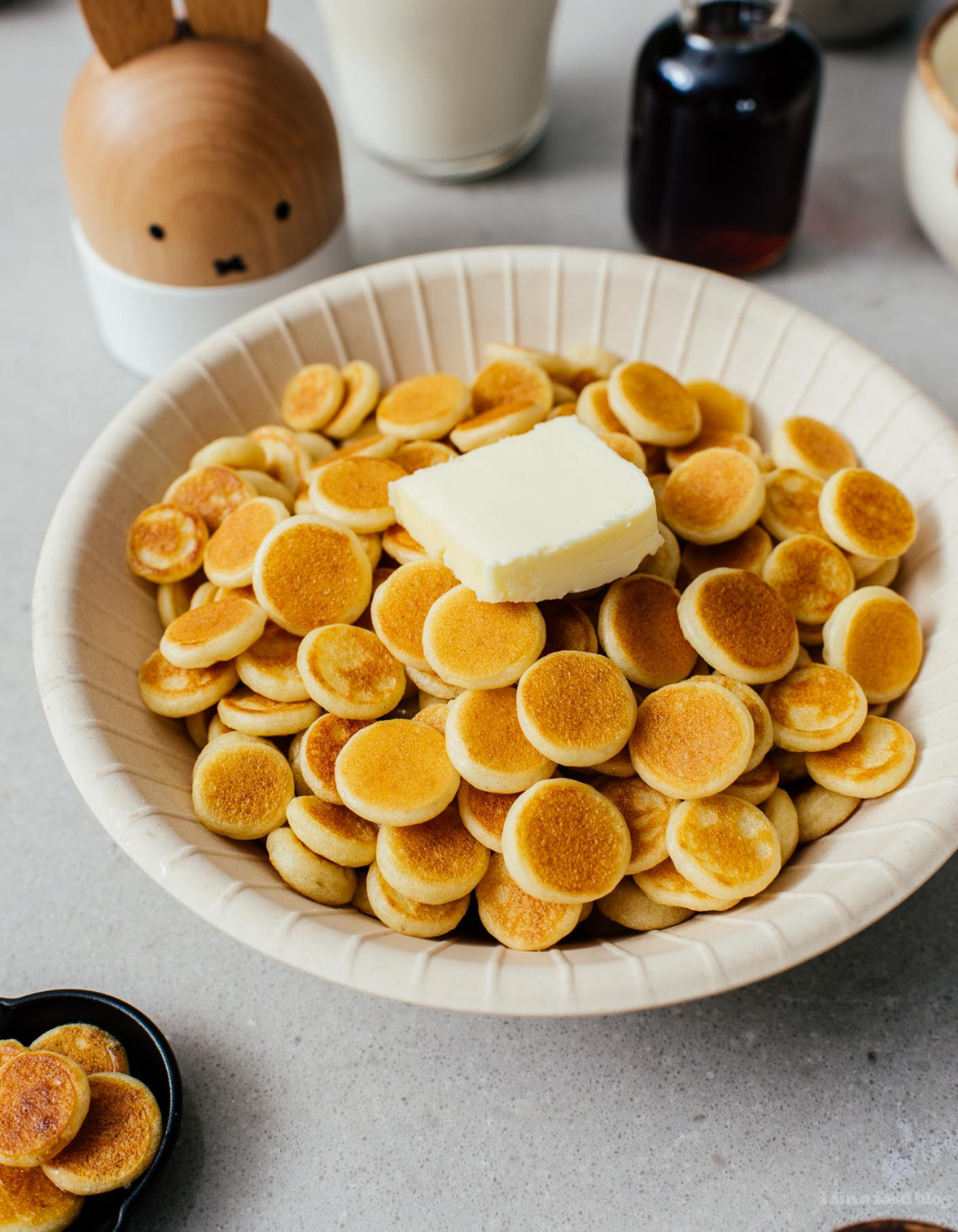 a bowl of very small pancakes, about the size of a quarter, with a pad of butter sitting on top.