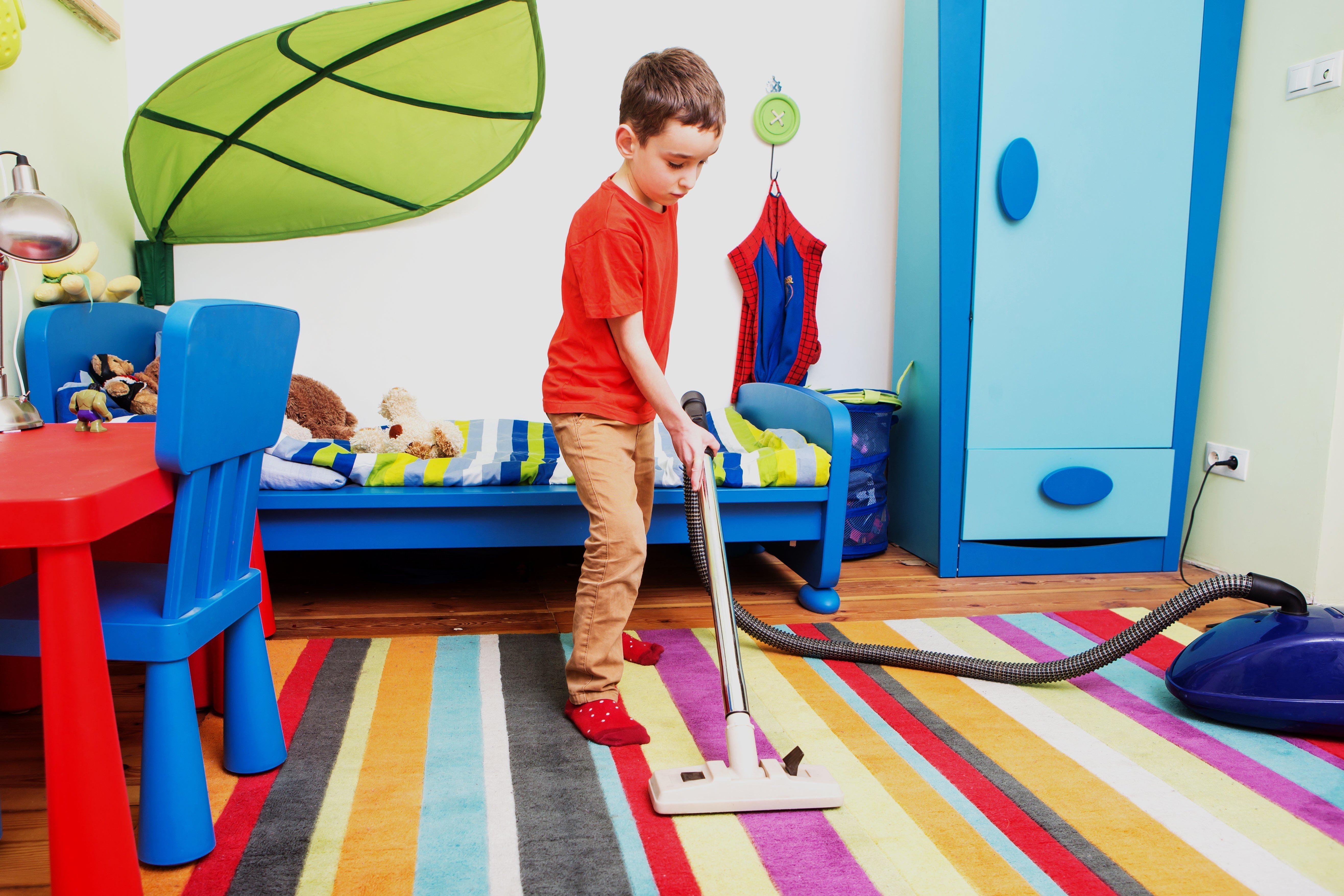 A young boy vacuums a colorful rug in a play room.