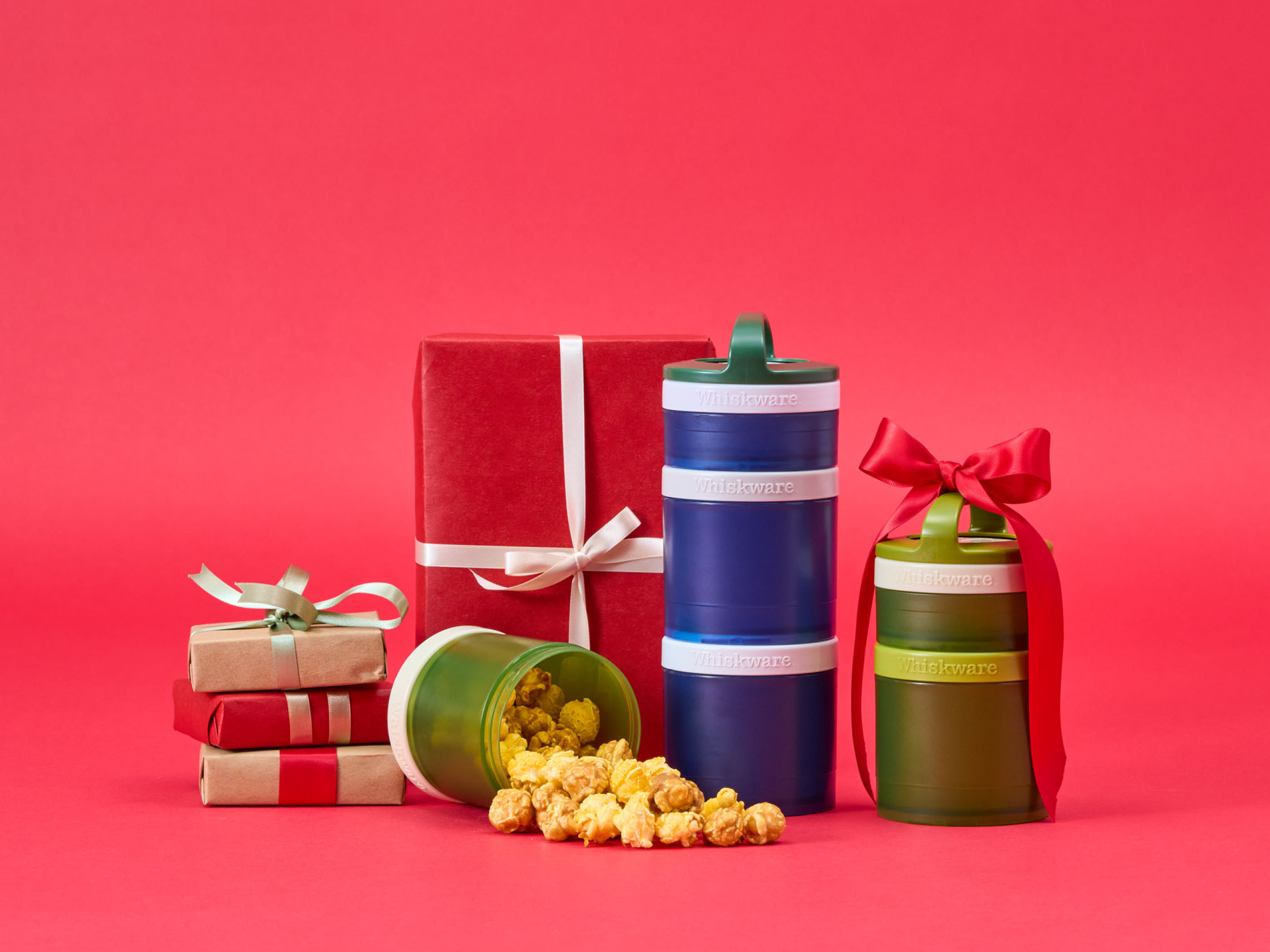 Whiskware containers filled with popcorn and wrapped gifts on a red background.
