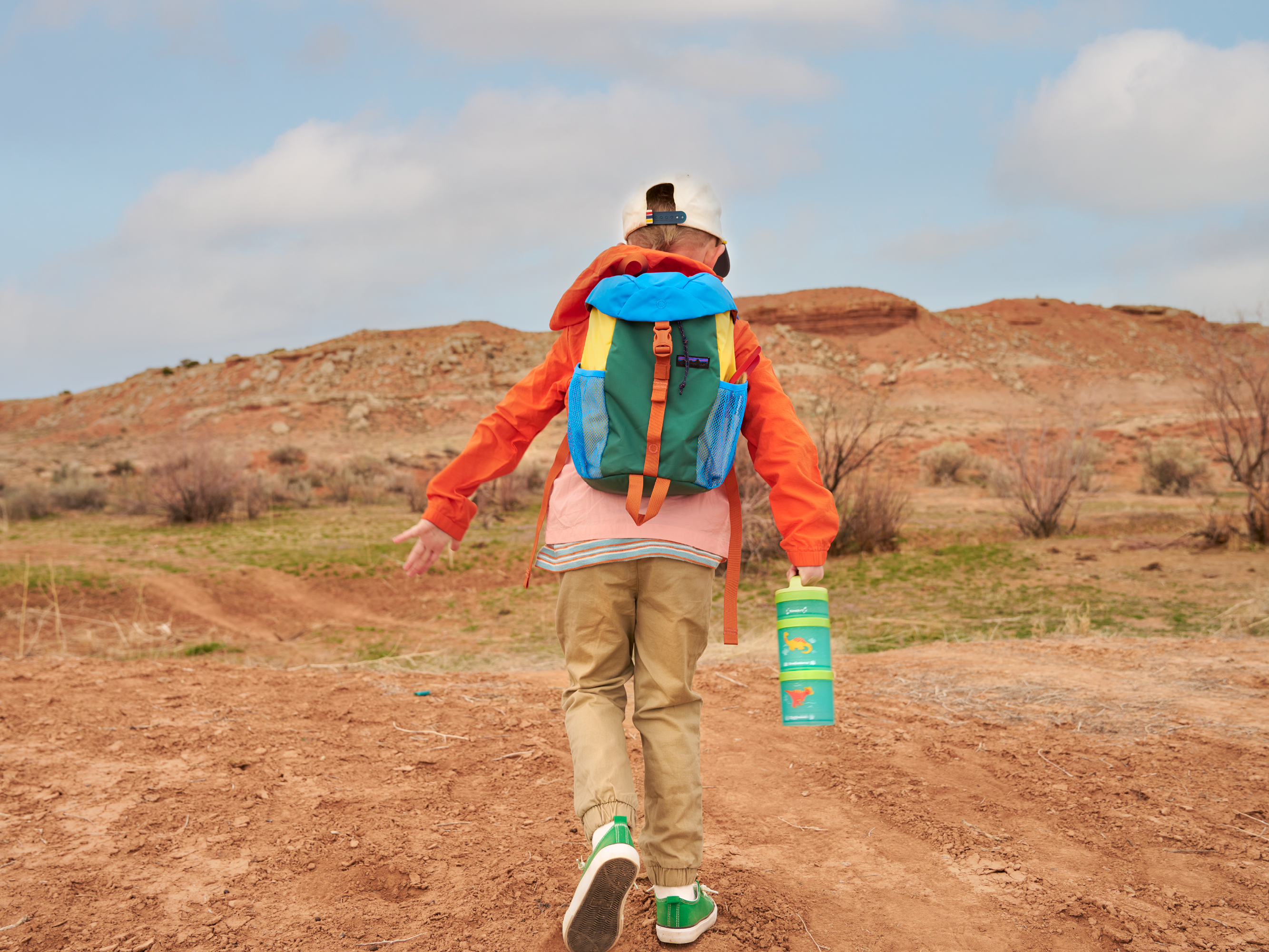 Boy with backpack and Whiskware snack container running on an outdoor red rock trail.