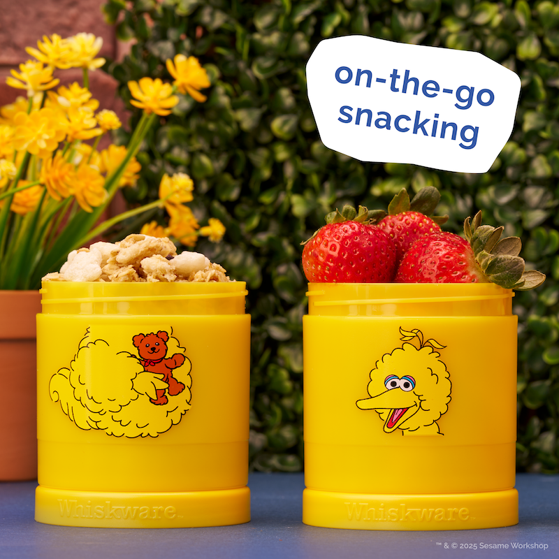 Yellow snack container filled with granola and strawberries in front of an outdoor garden background.
