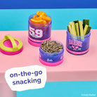 Barbie-themed snack containers with snacks on a colorful background, featuring the text 'on-the-go snacking'.
