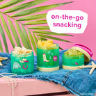 Barbie-themed snack containers filled with fruit and popcorn on a colorful background, featuring the text 'on-the-go snacking'.