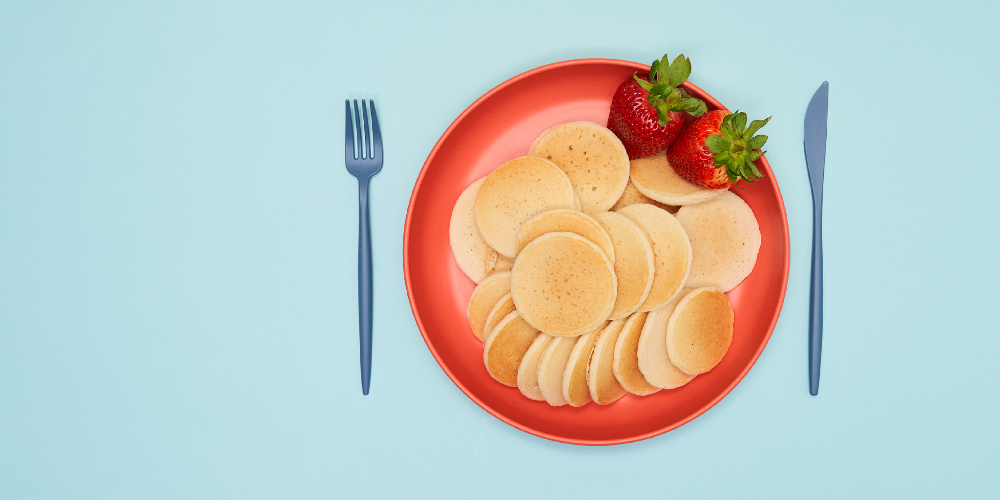 Red plate with pancakes and strawberries on a light blue background