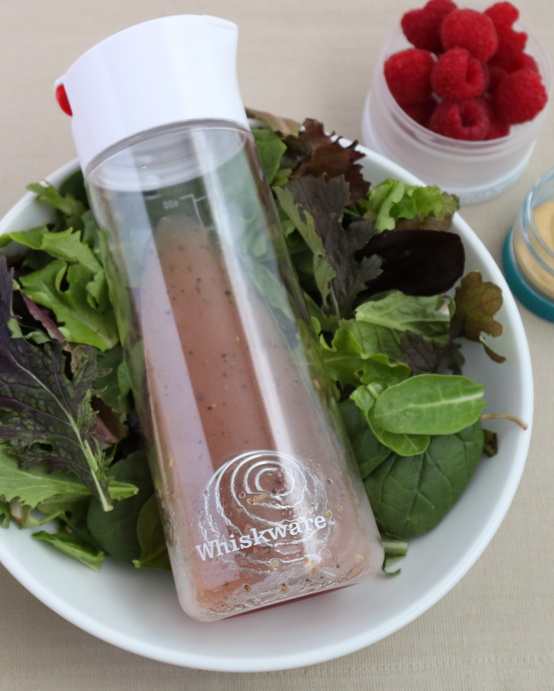 A whiskware dressing shaker laying on a bed of lettuce.