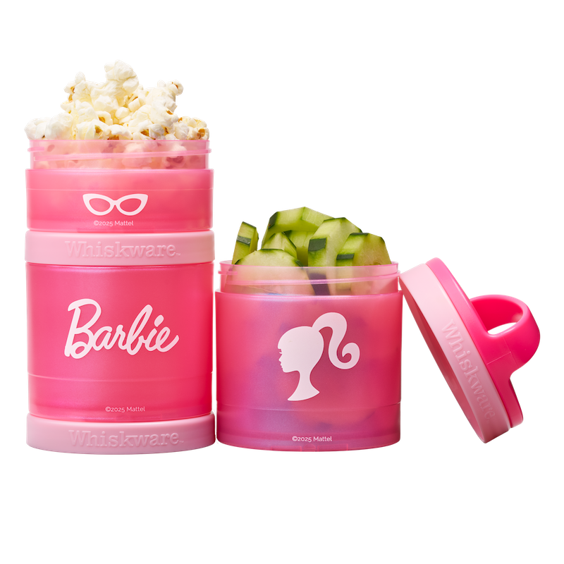 Two pink snack containers with Barbie logo, one filled with popcorn and the other with cucumbers.