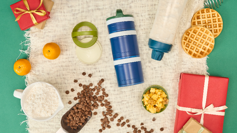 Assorted items including a blue snack container, waffles, oranges, and a gift box on a textured surface.